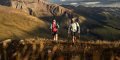 Zwei Wanderer bei Sonnenuntergang, im Hintergrund sind imposante Berge - Link zu Wandern