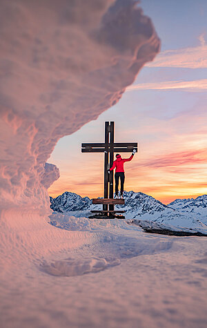 Schneeschuhwanderer am Gipfelkreuz Schareck bei Sonnenuntergang