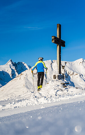 Mann blickt auf den Großglockner und steht dabei am Gipfelkreuz vom Schareck